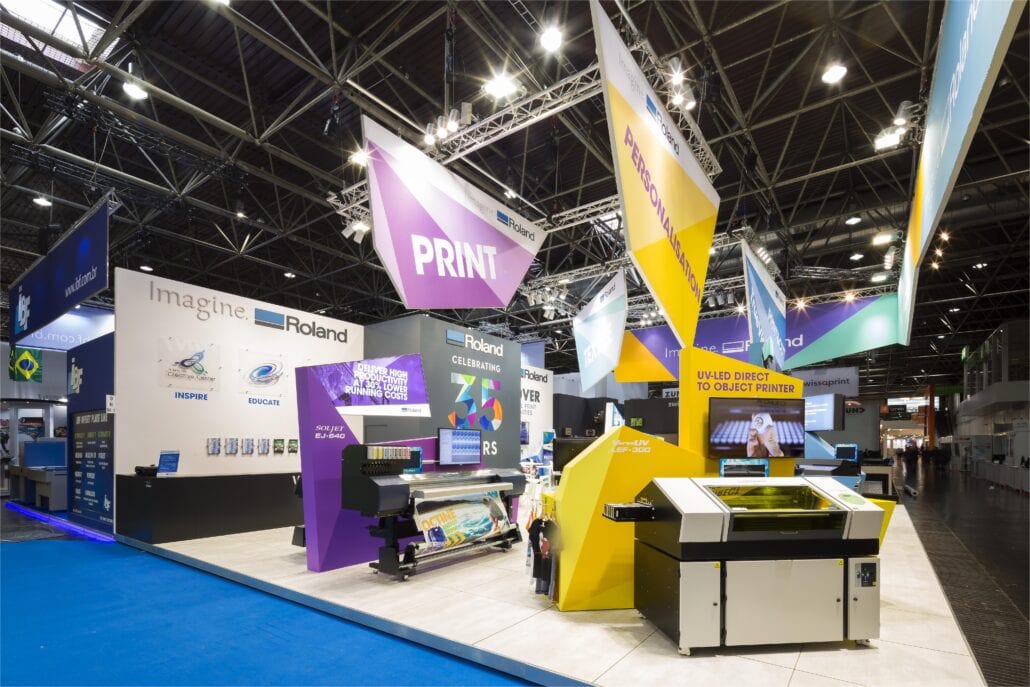 Alle elementen van deze beursstand zijn opgemaakt volgens een geometrisch patroon in verschillende kleurvlakken. kleurrijk zicht op de beursstand van Roland Dg op Drupa Dusseldorf