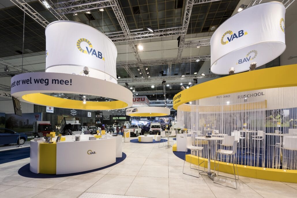 De ronde vormen van het logo vertaald in een prachtige beursstand op het Autosalon. Expo Z standenbouw voorziet ook huur van beursmeubilair uit eigen beheer. rigging en banners op de beursstand van VAB op Autosalon Brussel