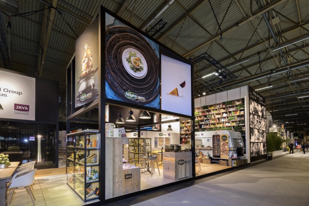 Grote prints hoog in de lucht zorgen voor een goede zichtbaarheid op de stand van Sligro op Horeca Expo te Gent. torens met grote prints op de beursstand van Sligro op Horeca Expo te Gent