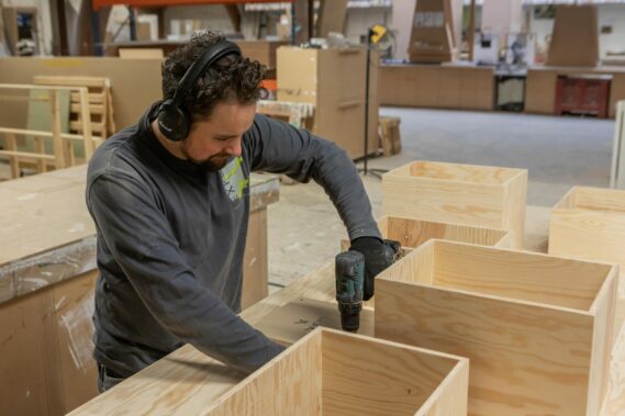 Uw op maat gemaakte houtbouw beursstand wordt door onze ervaren standebouwers tot in de puntjes voorbereid in ons atelier in Westmalle. standenbouwer met een schroefmachine aan het werk aan een beursstand